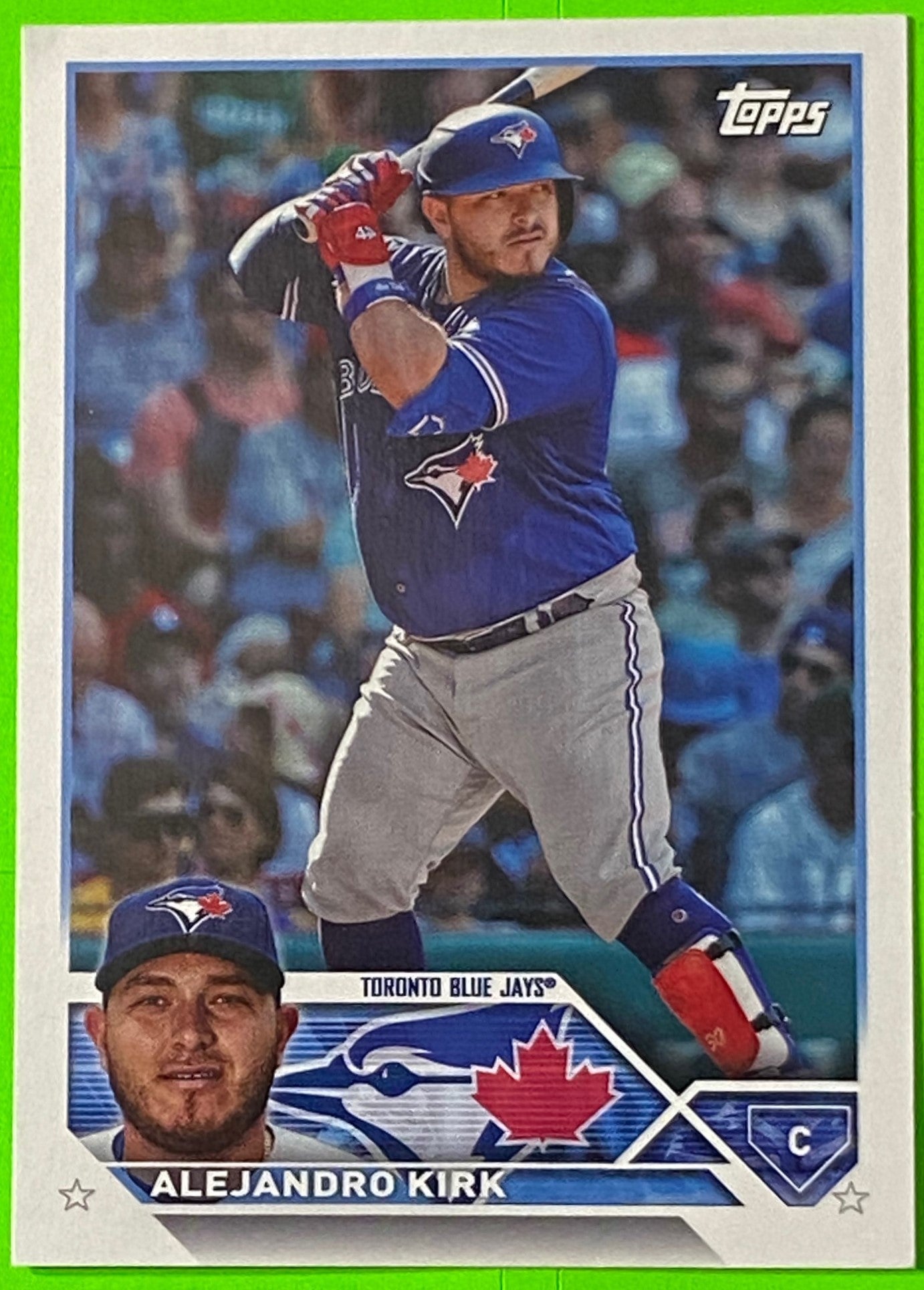 A collectible baseball card featuring Toronto Blue Jays player Alejandro Kirk in a blue uniform, with a smaller photo of him in a grey uniform on the card's lower left corner.