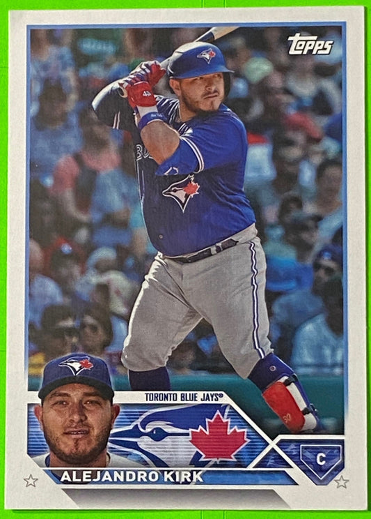 A collectible baseball card featuring Toronto Blue Jays player Alejandro Kirk in a blue uniform, with a smaller photo of him in a grey uniform on the card's lower left corner.